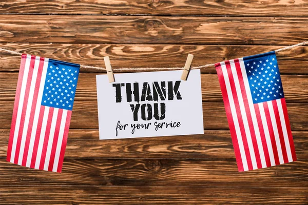Card for veterans day hanging on string with pins and american flags on wooden background — Stock Photo