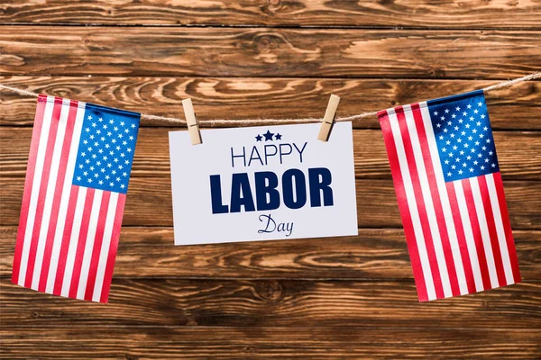 Card with happy labor day lettering hanging on string with pins and american flags on wooden background — Stock Photo