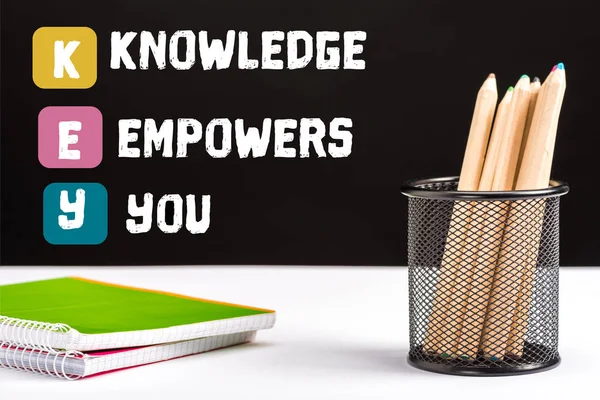 Notebooks and color pencils on table with key and knowledge empowers you lettering on black — Stock Photo