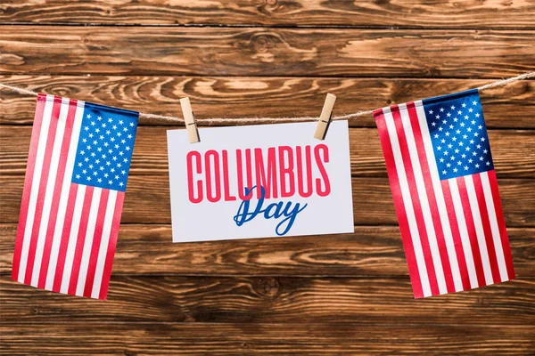 Card with Columbus day lettering hanging on string with pins and american flags on wooden background — Stock Photo