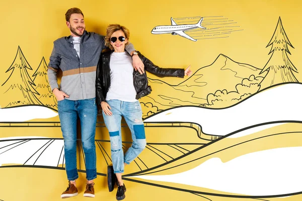 Happy woman showing thumb up and hugging boyfriend with mountains and airplane illustration on yellow background — Stock Photo