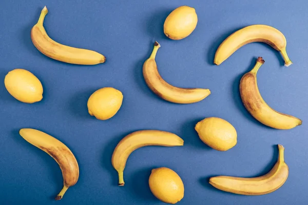 Склад їжі з лимонами та стиглими бананами, що лежать ізольовано на синьому фоні — стокове фото
