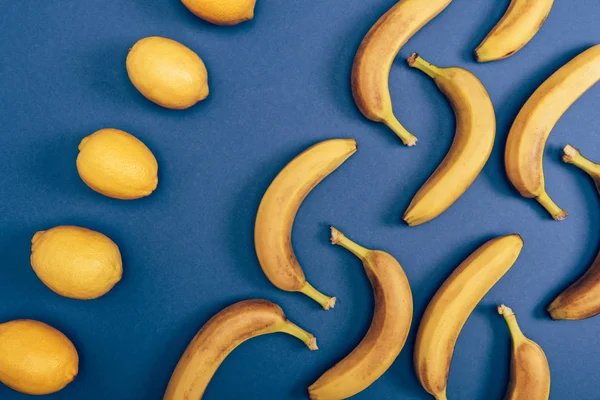 Вид сверху сочных и желтых лимонов и ярких бананов на синем фоне — стоковое фото