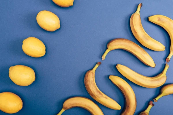 Ansicht von oben mit gelben Zitronen und frischen Bananen auf blauem Hintergrund — Stockfoto