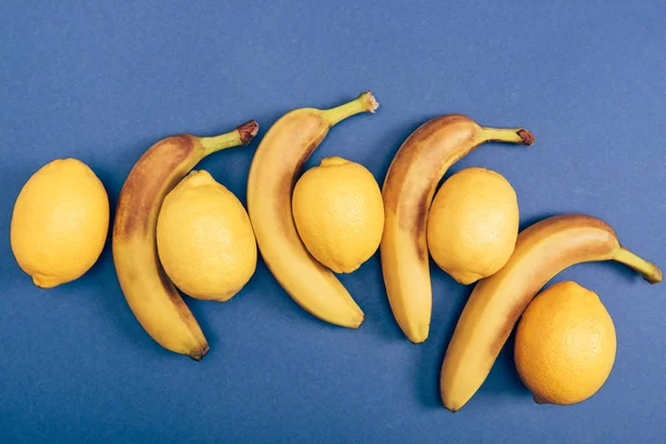 Vista dall'alto di limoni brillanti e gialli con banane su sfondo blu — Foto stock