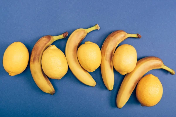 Top view of bright and yellow lemons with bananas on blue background — Stock Photo