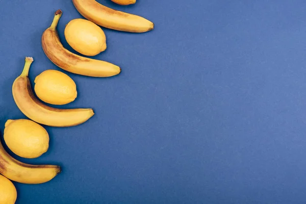 Top view of yellow lemons and bananas on blue background with copy space — Stock Photo