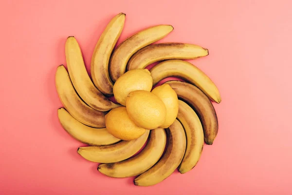 Вид зверху на харчовий склад жовтих органічних бананів і лимонів на кораловому фоні — стокове фото