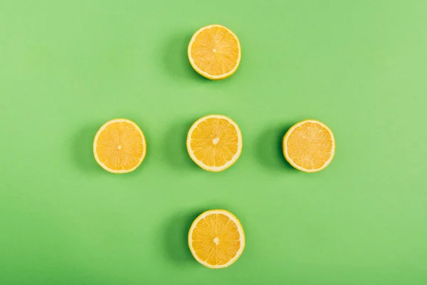 Вид сверху на желтые и вкусные нарезанные лимоны на цветном зеленом фоне — стоковое фото