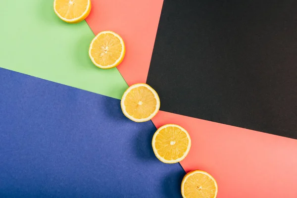 Top view of fresh and yellow cut lemons on multicolored black blue green coral background — Stock Photo