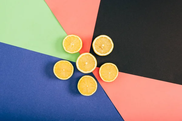 Top view of bright yellow cut lemons on multicolored black blue coral green background — Stock Photo
