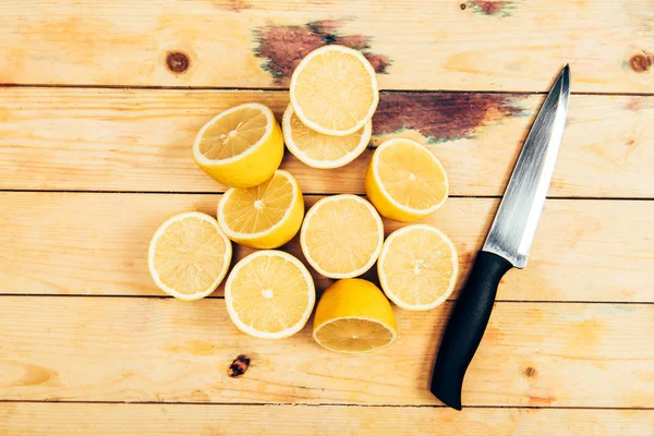 Top view of bright yellow cut lemons with knife on wooden table background — Stock Photo