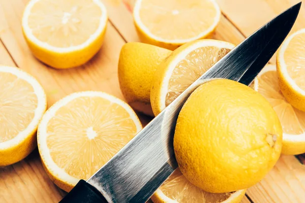 Close up view of fresh and yellow cut lemons with knife on wood surface — Stock Photo