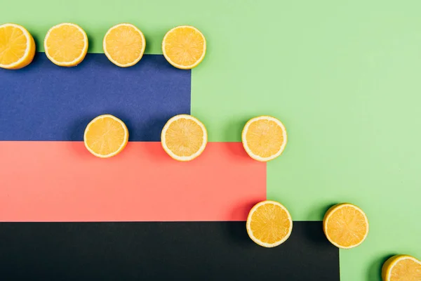 Vista dall'alto di deliziosi, succosi e gialli limoni tagliati su sfondo multicolore verde, corallo, blu, nero — Foto stock