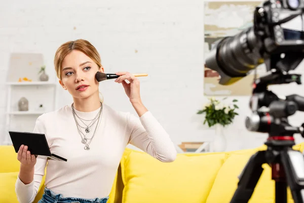Beauty blogger sitting on yellow sofa and doing makeup in front of video camera — Stock Photo