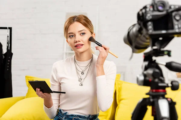 Blogueur beauté assis sur le canapé jaune et faire du maquillage devant la caméra vidéo — Photo de stock