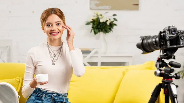 Smiling beauty blogger applying face cream in front of video camera — Stock Photo