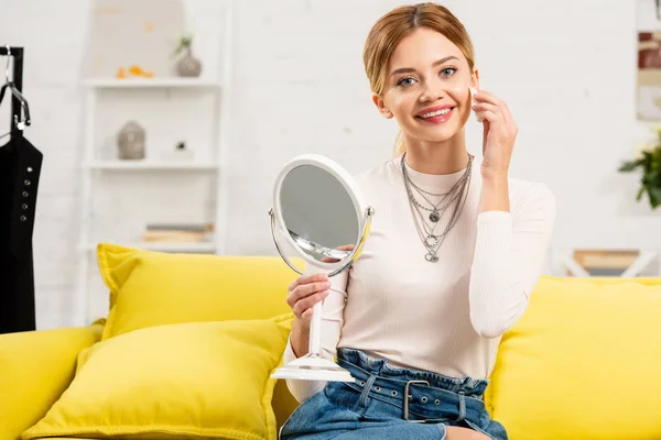 Улыбающийся блоггер красоты с зеркалом с использованием декоративной косметики перед видеокамерой — стоковое фото