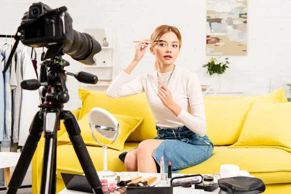 Beauty blogger in denim skirt doing eyebrows in front of video camera — Stock Photo