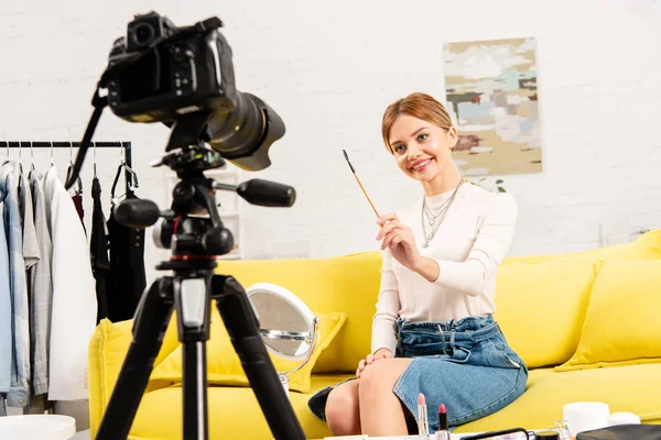 Smiling beauty blogger holding cosmetic brush in front of video camera — Stock Photo