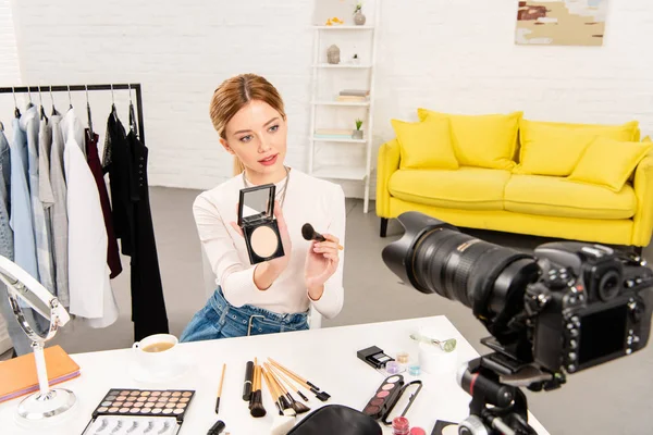 Beauty blogger showing face powder and cosmetic brush in front of video camera — Stock Photo