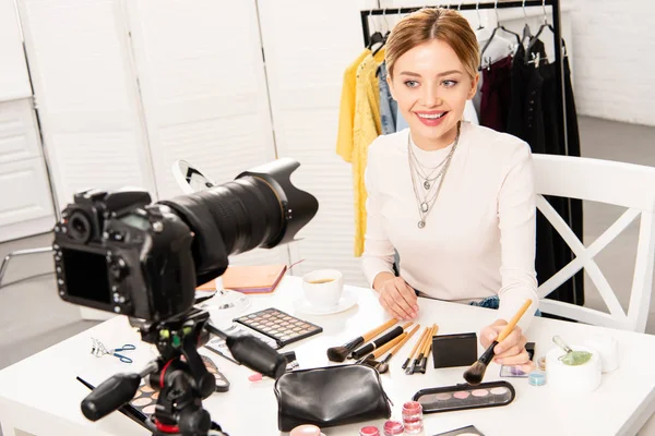 Blogueiro de beleza com cosméticos decorativos olhando para câmera de vídeo com sorriso — Fotografia de Stock