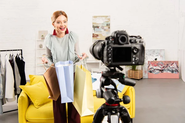 Smiling blogger holding shopping bags in front of video camera at home — Stock Photo