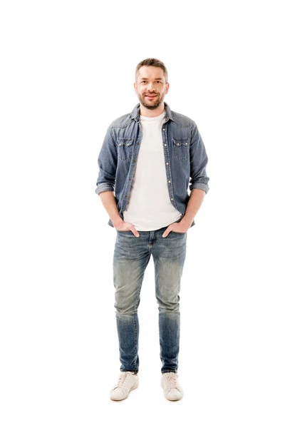 Полный вид улыбающегося бородатого человека в джинсах, стоящего с руками в карманах, изолированных на белом — стоковое фото