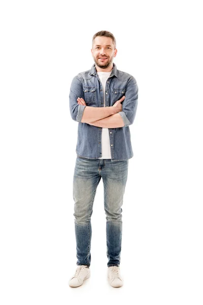 Vista completa de hombre barbudo sonriente en jeans de pie con brazos cruzados aislados en blanco - foto de stock