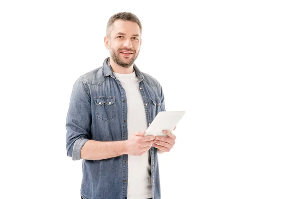 Hombre barbudo sonriente en camisa vaquera usando tableta digital y mirando a la cámara aislada en blanco - foto de stock