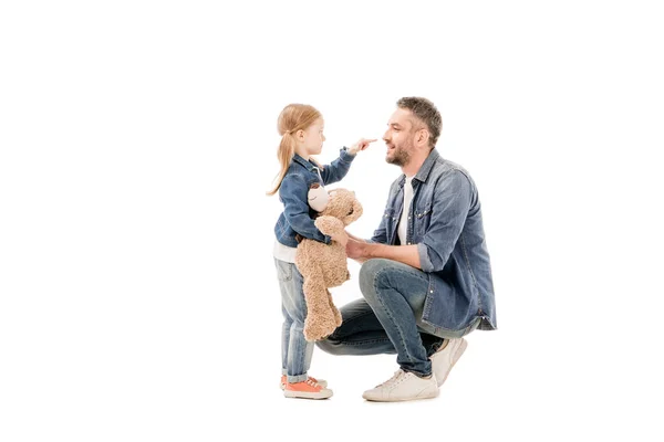 Vista lateral de la hija con oso de peluche y papá barbudo mirándose aislados en blanco - foto de stock