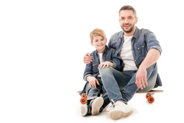 Son and dad sitting on skateboard and embracing on white — Stock Photo