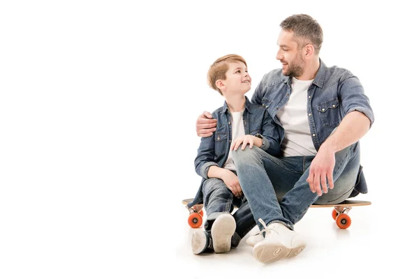 Син і тато сидять на скейтборді і обіймаються на білому — стокове фото