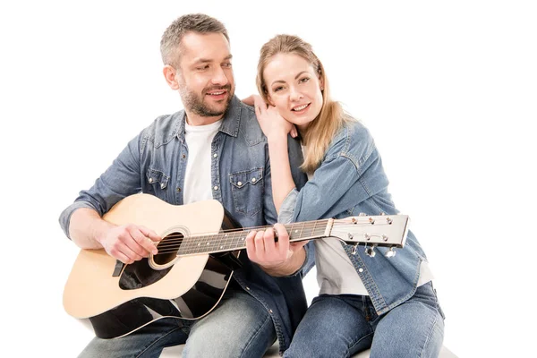 Smiling man in jeans playing acoustic guitar for wife isolated on white — Stock Photo
