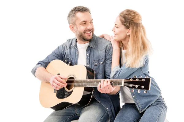 Homem sorridente em jeans tocando guitarra acústica para esposa isolada em branco — Fotografia de Stock