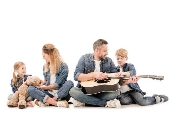 Щаслива сім'я в джинсах з плюшевим ведмедем і акустичною гітарою, сидить ізольовано на білому — стокове фото