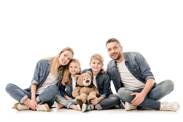 Família feliz em jeans com ursinho sentado isolado no branco — Fotografia de Stock