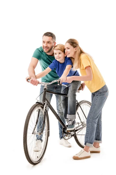 Vista completa de los padres sonrientes enseñando a su hijo a andar en bicicleta aislado en blanco - foto de stock