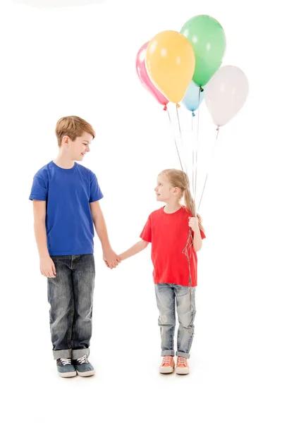 Vista a tutta lunghezza di due bambini con palloncini colorati che tengono le mani isolate sul bianco — Foto stock