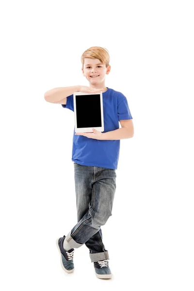 Повний вигляд усміхненого хлопчика в синій футболці, що тримає цифровий планшет з порожнім екраном ізольовано на білому — стокове фото