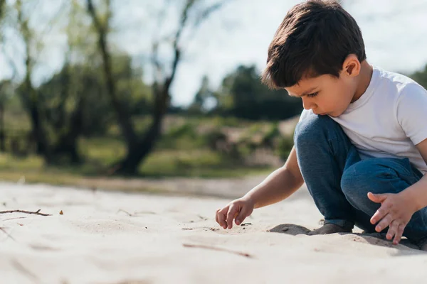 かわいい男の子が座って砂を見て — ストック写真