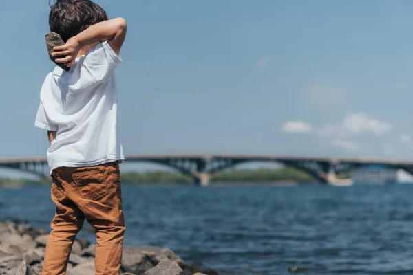 Back View Cute Boy Holding Rock Blue Lake — Stock Photo, Image