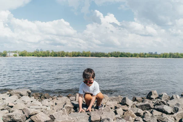 Stylish Boy Sunglasses Touching Rock While Sitting Lake — Stock Photo, Image