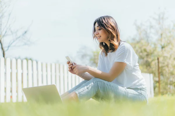 Selective Focus Happy Woman Using Smartphone Laptop While Sitting Grass — Stock Photo, Image