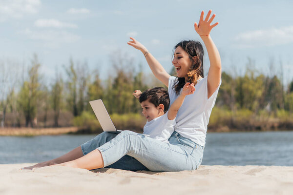 selective focus of happy mother and son with hands above head looking at laptop