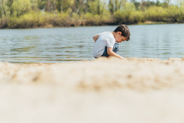 selective focus of cute boy sitting near pond 