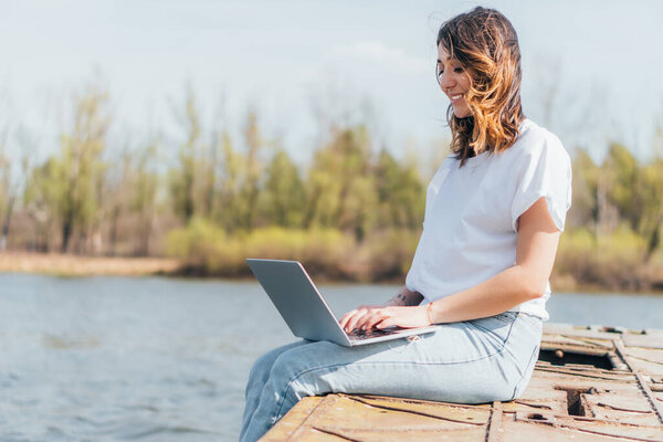 happy freelancer smiling and using laptop near river 