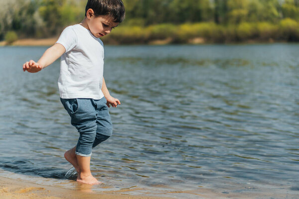 adorable child walking near lake and looking at water