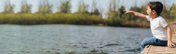 Website Header Emotional Boy Pointing Finger While Sitting River — Stock Photo, Image