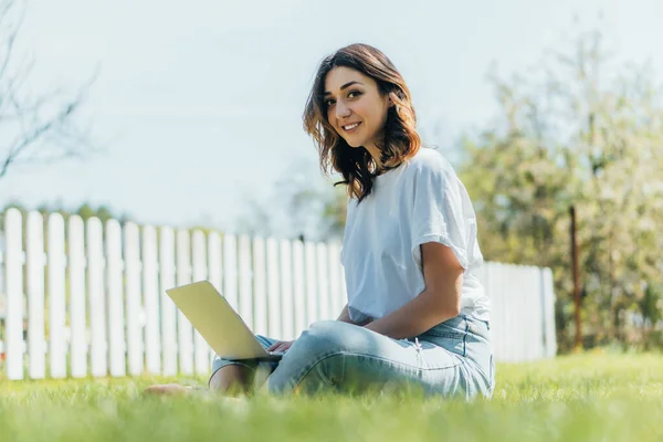 Fokus Selektif Wanita Tersenyum Menggunakan Laptop Dan Duduk Rumput Stok Gambar